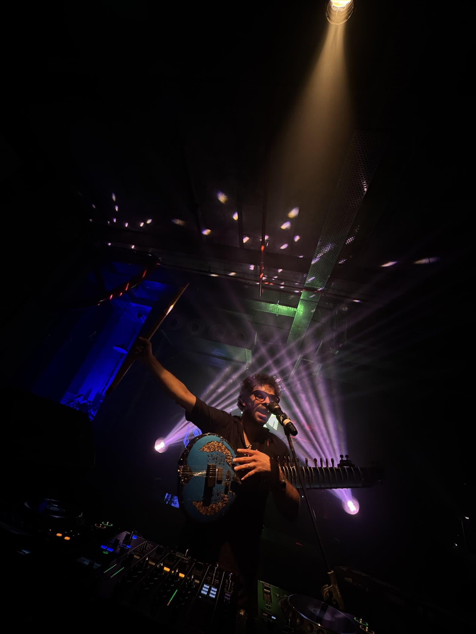 Akhlad Ahmed performing live under a spotlight with sitar and mic